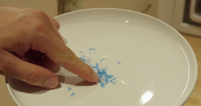 Close-up of hand showing microplastic particles on a plate.