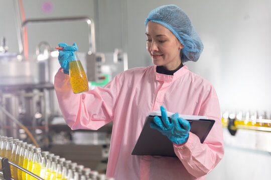 Young beautiful  white woman inspector standing in front of assembly line with capped bottled drinks and examining plastic packaging.