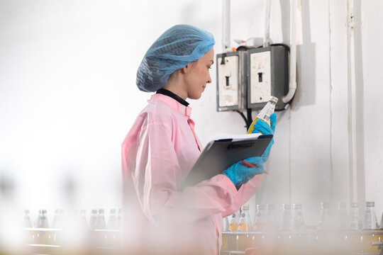 Young beautiful  white woman inspector standing in front of assembly line with capped bottled drinks and examining plastic packaging.