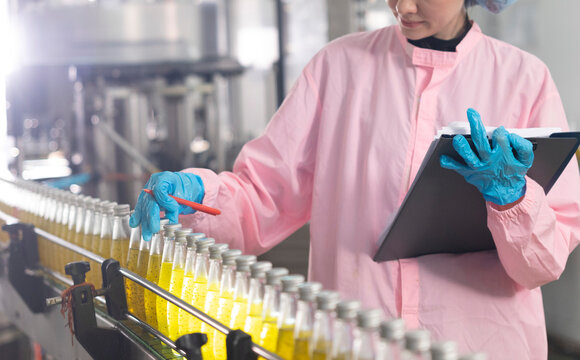 Young beautiful  white woman inspector standing in front of assembly line with capped bottled drinks and examining plastic packaging.