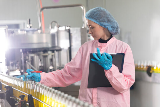 Young beautiful  white woman inspector standing in front of assembly line with capped bottled drinks and examining plastic packaging.