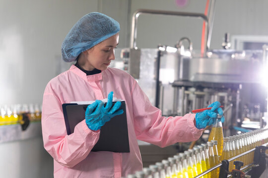 Young beautiful  white woman inspector standing in front of assembly line with capped bottled drinks and examining plastic packaging.
