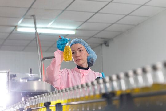 Young beautiful  white woman inspector standing in front of assembly line with capped bottled drinks and examining plastic packaging.
