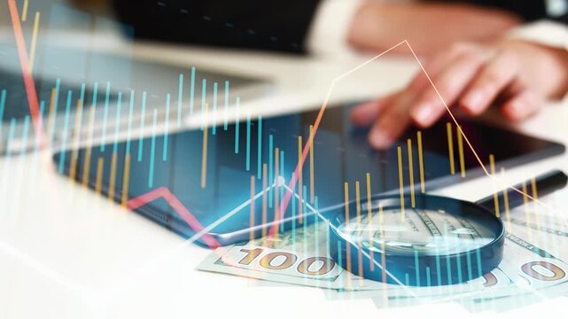 A person works with charts and graphs on a laptop while handling cash in a professional setting. Money is laid out on the table, showing interest in finance and investment.