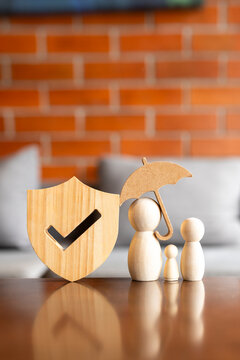 Family life insurance and healthcare protection concept with wooden shield and peg doll figures under umbrella on table for child safety, domestic welfare guarantee and health policy.