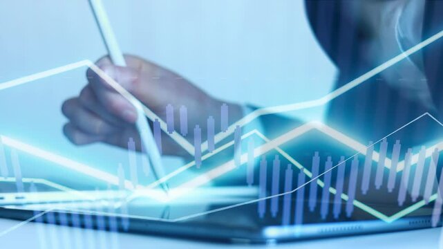 A person is using a stylus to write on a tablet. There are digital graphs and data displayed, showing financial trends. The scene takes place in a modern office environment.