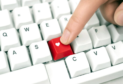Closeup of a finger pressing a red keyboard key with heart symbol for love concept