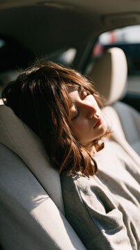 A woman sleeping in a modern car interior with the sunlight on her face, it is travel lifestyle visual emphasizing comfort and relaxation.