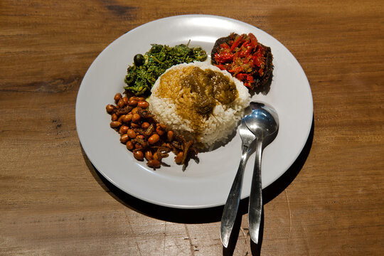 A plate of typical Nasi Padang on wooden table, popular spicy Indonesian dish with rice for lunch
