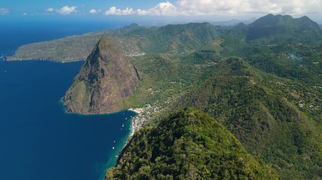 Aerial tilt shot rises above Gros Piton revealing volcanic peak coastal village and deep blue bay in Saint Lucia