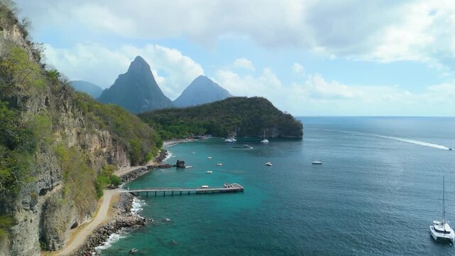 Aerial view along rugged coastline reveals Anse Chastanet Beach turquoise bay and twin Piton peaks in Saint Lucia