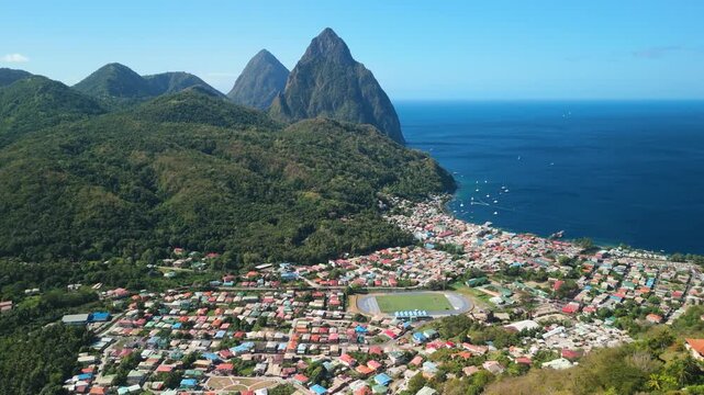 Aerial shot slowly pulls back revealing colorful Soufriere town coastline and twin Piton peaks in Saint Lucia