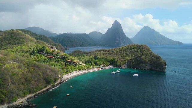 Aerial panning shot reveals Anse Chastanet Beach resort cove and misty Piton peaks in background Saint Lucia