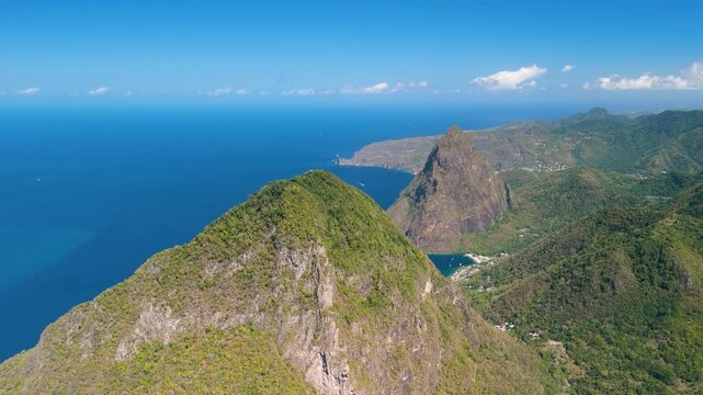 Aerial view reveals Gros Piton and Petit Piton rising above deep blue sea with coastal village nestled between peaks