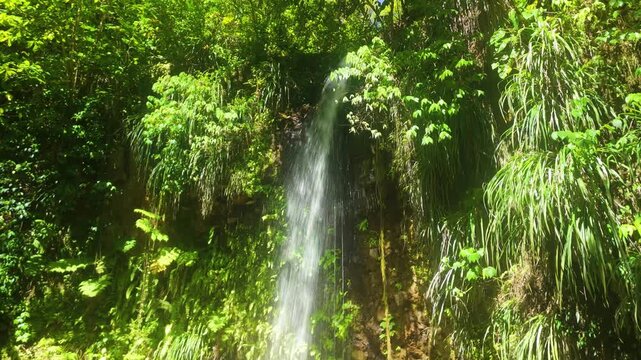Slow aerial approach reveals Toraille Waterfall cascading down rocky cliff surrounded by lush tropical rainforest in Saint Lucia