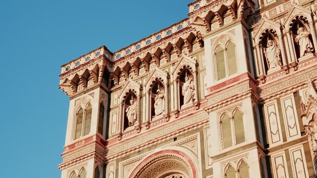 Tiers of carved saints and inlaid marble panels surround the traceried rose window of Florence Cathedral in Tuscany. Ground level close detail shot, slow rising move.