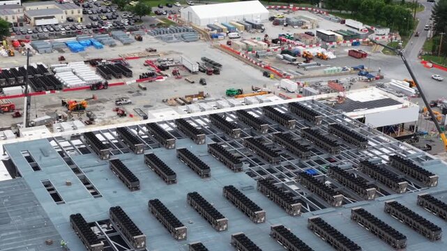 Rooftop cooling units go in by the row at a data center under construction in Lancaster, Pennsylvania, cranes, telehandlers and a laydown yard of pipe below. Aerial flyover shot