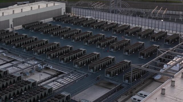Dry cooler banks cover the roof of an Ashburn, Virginia data center, rows of white storage tanks and chilled water pipes lining the wall below. Aerial lateral wide shot