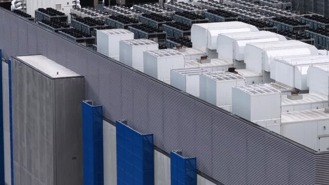 The view rises past a blue and grey panelled wall in Clifton, New Jersey to reveal a screened rooftop yard packed with condensers and air handling units. Aerial rising shot