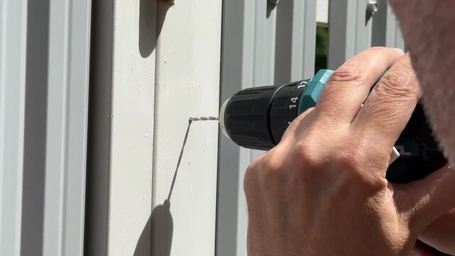 A close-up shot of a hand with a power drill punching through a metal fence post. Original audio. Video from a photo bank. High quality FullHD footage