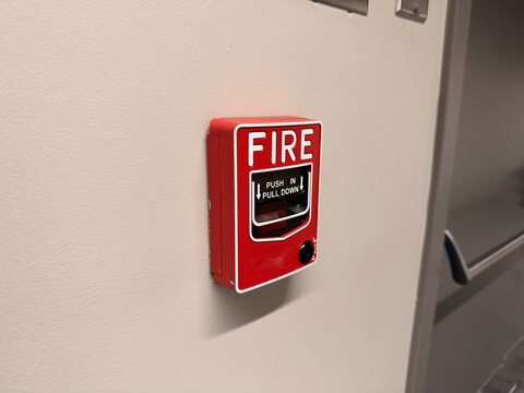 Red fire alarm pull station mounted on white wall indoors