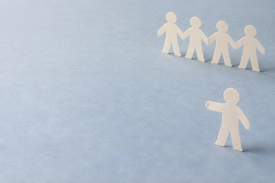 Abgetrennte Papierfigur vor einer Menschenkette als Symbol f&uuml;r soziale Ausgrenzung