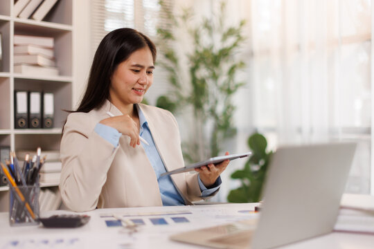 Young asian businesswoman analyzing data and managing tasks on a digital tablet, working in a modern office, showing productivity and efficiency in her professional career