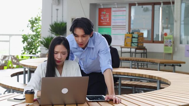 Two Asian Business Colleagues Collaborating and Discussing Work on Laptop