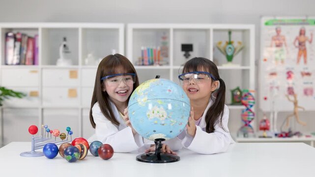Two Young Students in Lab Coats Examining a Globe in Science Classroom