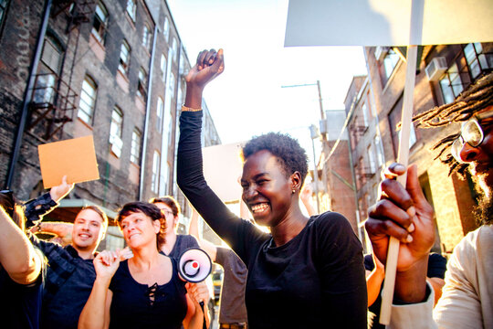 Diverse group of people holding signs and a megaphone, smiling during a protest.