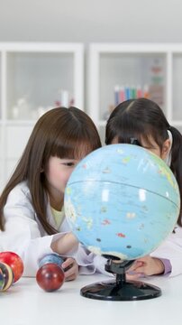 Two Young Schoolgirls in Lab Coats Studying a World Globe