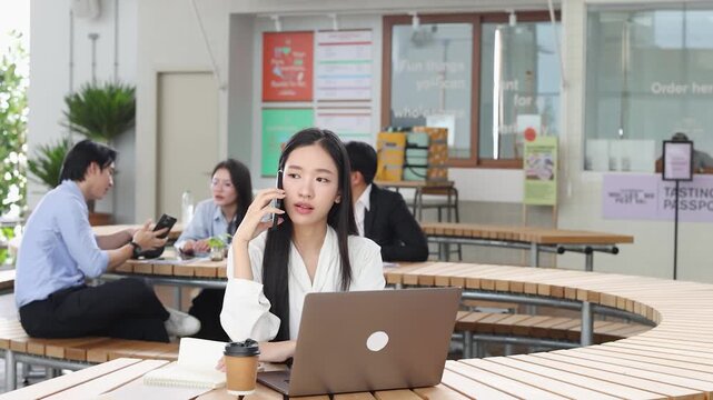 Thai Businesswoman Talking on Smartphone While Working on Laptop in Bangkok