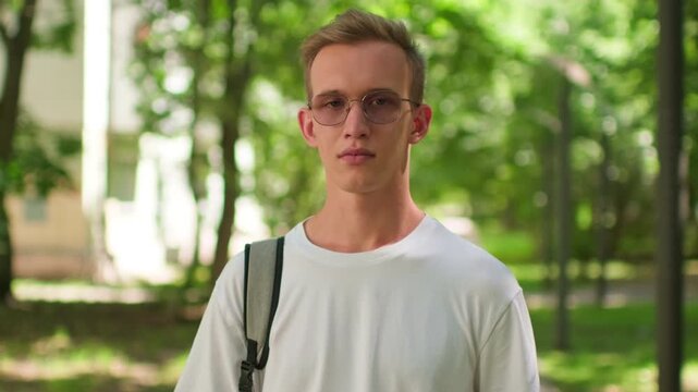 Student with a backpack and glasses on university campus. Man enjoying outdoor campus life in college. Young man wearing glasses and a backpack standing outside.