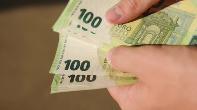 Counting 100 cash bills.Counting green banknotes outdoors on a sunny day. Man paying with Euro bills, flipping cash finance wealth concept.