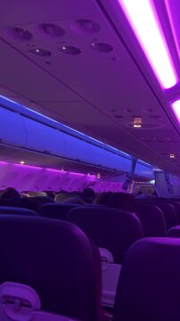 Interior of an airplane with purple and blue lighting. Passengers are seated, creating a cozy atmosphere. The scene captures modern air travel.