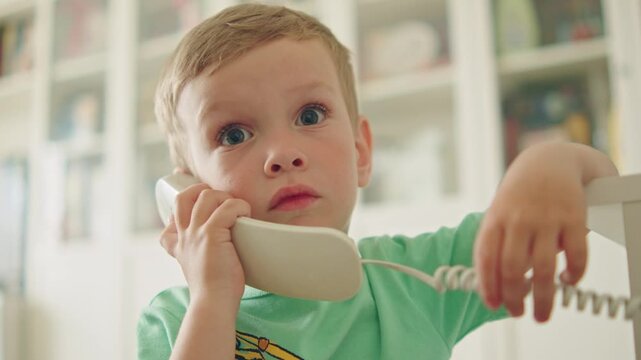Portrait of a young child listening through a retro corded phone. Cute little boy talking on a classic landline telephone at home.  Close up of a happy small kid talking with an old white phone.