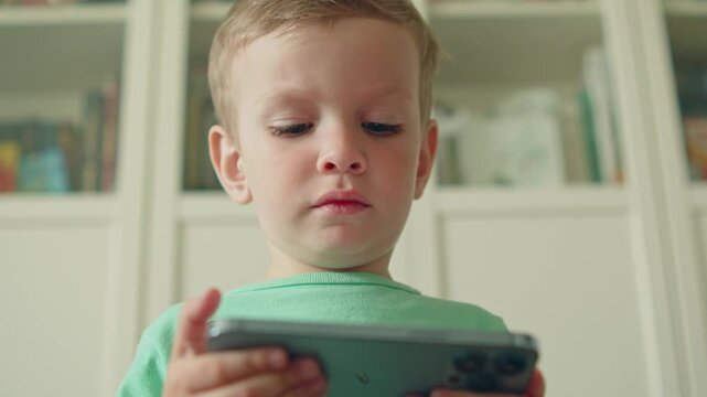 Little child watching an educational video on an Phone. Close-up of a small boy looking at a smart phone screen. Small kid watching a video on a gadget. 