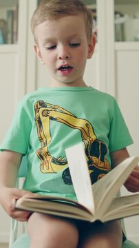 Cute little boy reading a book in a library. Child looking through a book with interest. Small kid flipping through pages in a big book. Vertical video