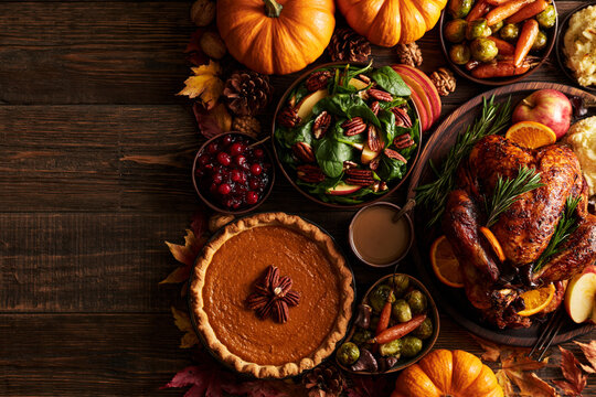 Thanksgiving feast overhead flat lay with roasted turkey, pecan pumpkin pie, mashed potatoes and sides on wooden table