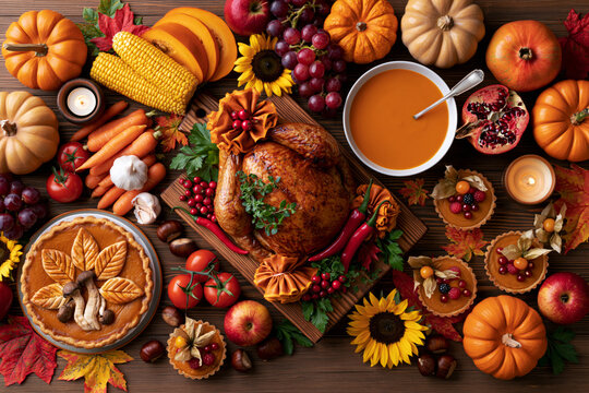 Abundant Thanksgiving spread overhead with roasted turkey, pumpkin pie, soup, pumpkins, corn and fruit