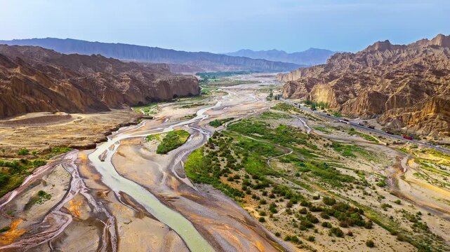Aerial scenic panorama of a winding riverbed and highway traversing a dry canyon in Xinjiang, China