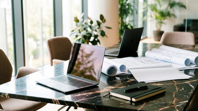 Modern office conference table with open laptop, architectural blueprints and notebook, professional business workspace