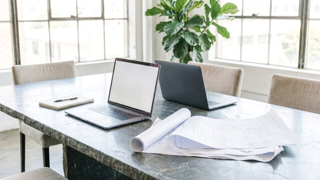 Modern office conference table with open laptop, architectural blueprints and notebook, professional business workspace