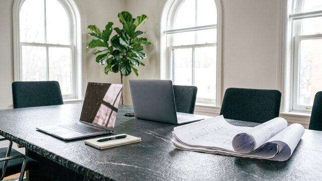 Modern office conference table with open laptop, architectural blueprints and notebook, professional business workspace