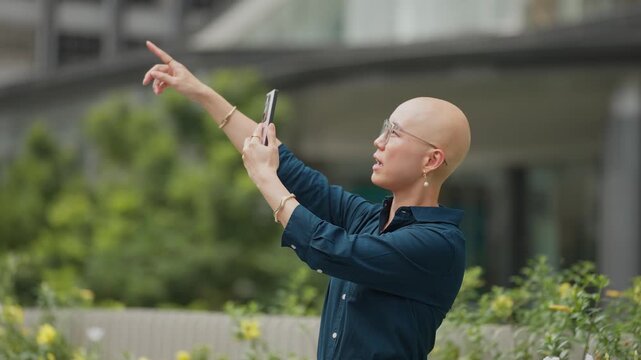 Calm woman points while filming outdoors. She wears glasses and a dark shirt. Her expression is focused.