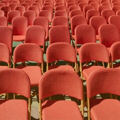 Fototapeta premium Coral folding chairs arranged in a precise symmetrical pattern on a driveway, featuring textured fabric and bright hard-edged lighting