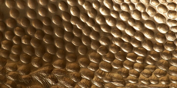 Embossed and hammered brass metal relief with a rich gold polished sheen, featuring a tactile dimpled surface for luxury backgrounds and material textures