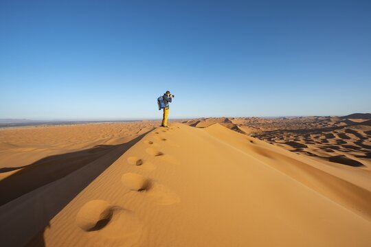 Young man standing on sand dune and photographed, Erg Chebbi, Merzouga, Sahara, Morocco