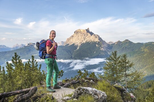 Young female hiker looks into the camera, behind her mountain peak La Rocheta, Dolomites, Belluno, Italy
