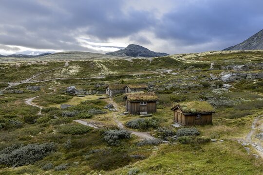 Wooden huts scattered in a forested mountain landscape with narrow paths and moderate cloud cover in the background, Peer Gynt hytta, Rondane National Park, Otta, Innlandet, Norway